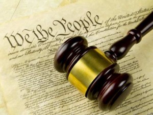 A wooden judge's gavel lies atop of a copy of the United States Constitution.