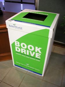 A large cardboard box with a hole in the top is labeled to accept donations for a book drive sponsored by the organization Better World Books.