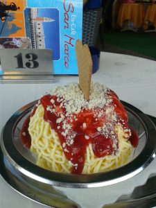 A plate of gelato ice cream shaped like spaghetti noodles and covered in red sauce.