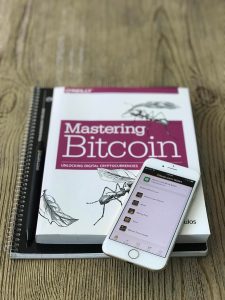Photo of a Bitcoin Cash wallet on a mobile phone and a copy of Mastering Bitcoin written by Andreas Antonopoulos