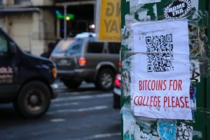 Photo of a lampost with a paper flyer taped to it asking passerby to send bitcoins to pay for college.