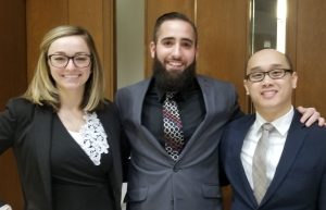 one woman and two men, all law students, stand before a courtroom door