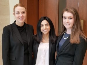 three women, all law students, stand in front of a courtroom door