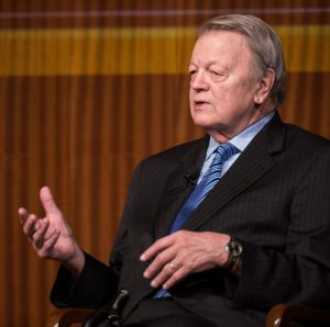 Author Garry Wills dressed in a suit and tie speaks at a public event.