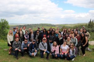 About 40 law students pose in casual clothes with the green hills of Israel in the background.