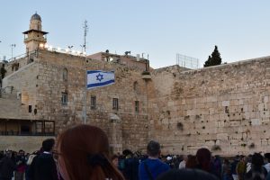 The Israeli flag flies in a courtyard outside of a brick building. 