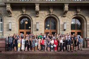 Large group of students and faculty standing on the steps of an official university building and posing for a group portrait.