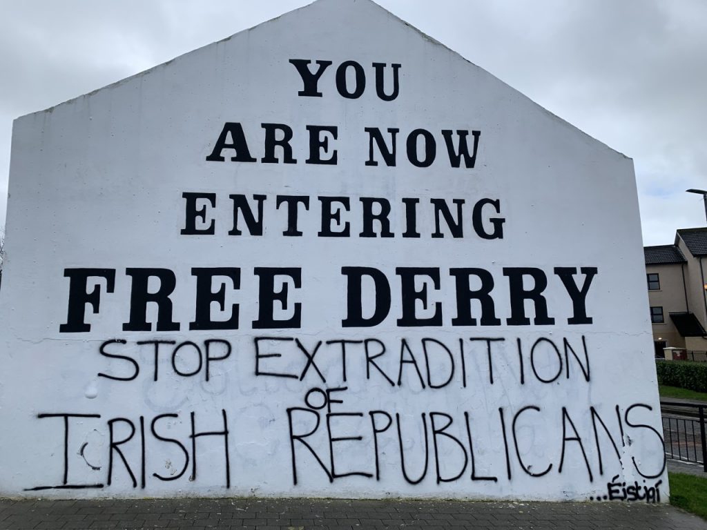 image of sign, it reads, "YOU ARE NOW ENTERING FREE DERRY" followed by the graffit "STOP EXTRADITION OF IRISH REPUBLICANS"