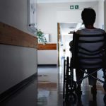 person sitting in wheelchair in empty nursing home hallway