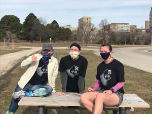 three women in running clothes sitting on or standing by a picnic table