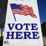 white sign with a picture of an American flag and the words "vote here."