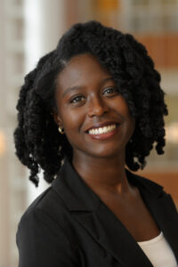 head shot of dark-skinned woman with curly hair and a big smile, wearing a white shirt and black suit jacket
