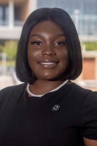 headshot of a dark-skinned woman with a sleek bob haircut wearing a black dress or coat with a pearl necklace