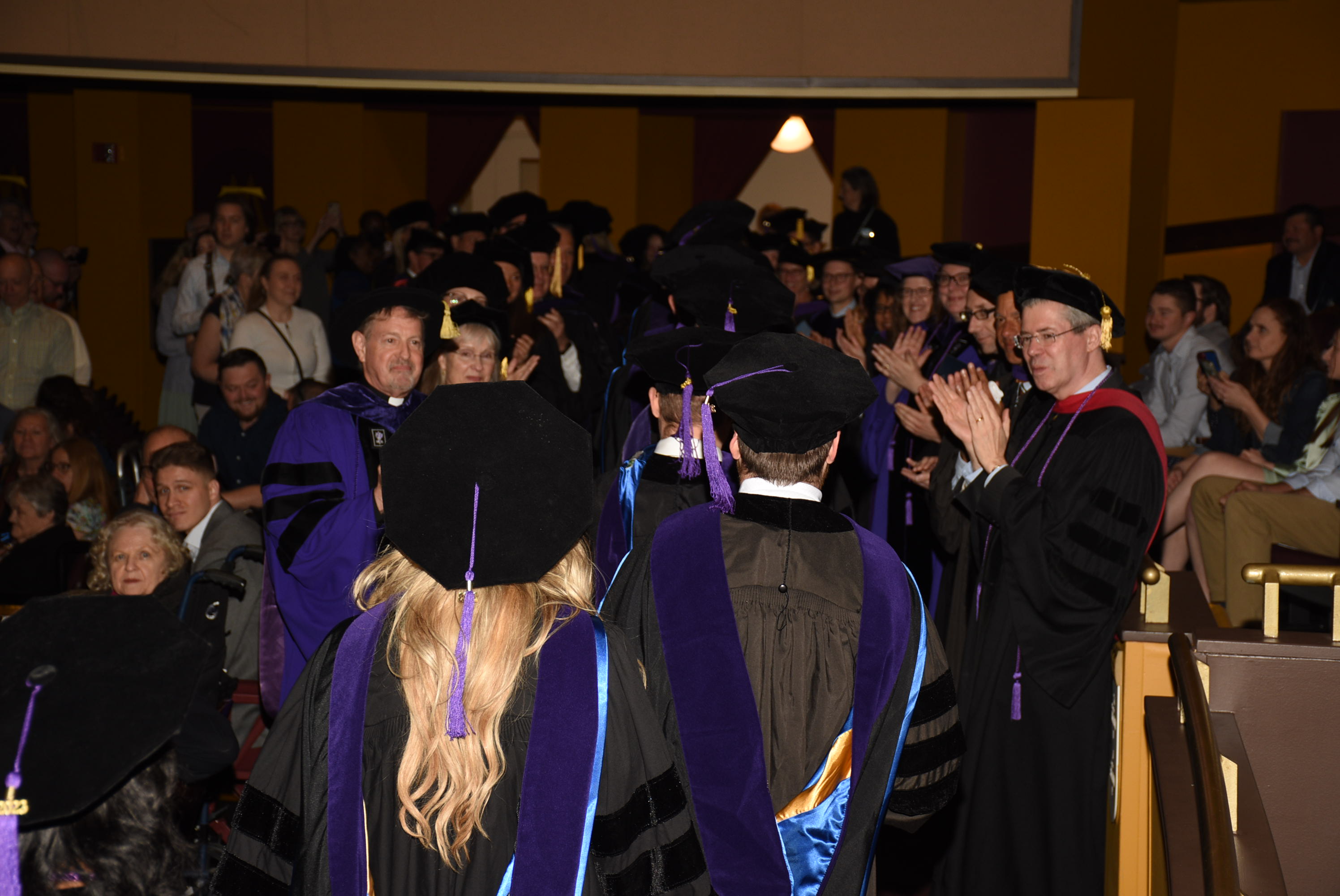 Faculty and guests cheer graduates on as they recess from the theatre. 
